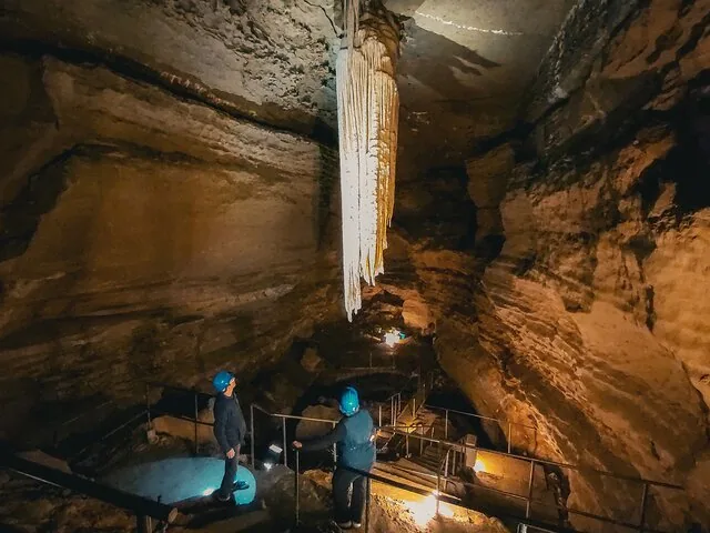 Personen betrachten den Großen Stalaktiten in der Doolin Cave, der von Licht angestrahlt wird.
