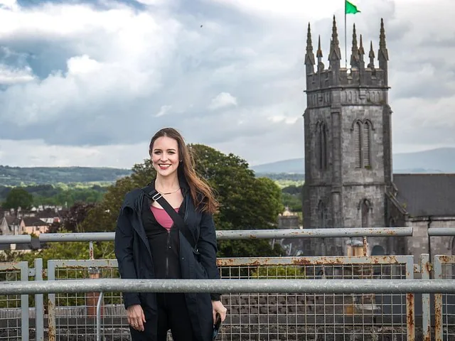 A smiling woman stands in front of a historic stone church tower.