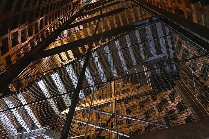 Looking up through a multi-level metal staircase structure enclosed in wire mesh.